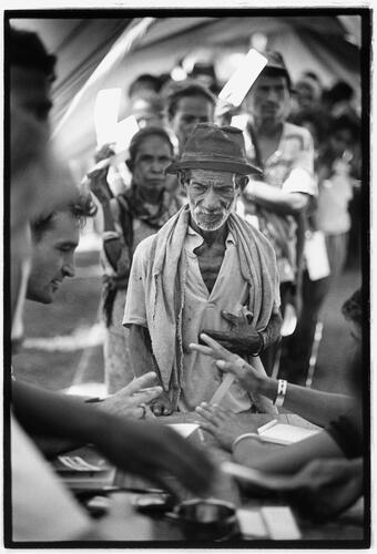 ***Warning! This item has been flagged and is undergoing a reviewing process due to its potentially sensitive content. Please refer to your communication and/or audiovisual referent prior to any possible internal or external use.*** 
 East Timor. Patients await treatment by a team of Medecins sans Frontieres (MSF)/Doctors without Borders in Dili stadium. Elderly man infront of table.