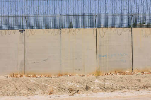 The Israeli Separation Wall cuts through the West Bank landscape. The 712-kilometer barrier remains the single largest physical obstacle directly impacting the daily movement and lives of 3.4 million Palestinians (OCHA).