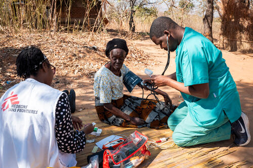 Wilfred Nkhambule, a palliative care nurse and Christina Banda, medical doctor,  with Doctors Without Borders (MSF), takes the blood pressure of Grace Nyambi, 72, outside her home in Chileka, in Blantyre district, on July 21, 2026. In care since April 2025, she suffers from abdominal pain; the team brings her morphine and fentanyl pain patches, laxatives and medication to control odor.
