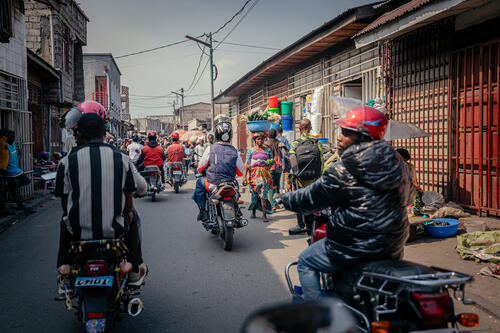 Des motards circulent dans le marché central de Birere, à Goma, à bord de leurs motos, à la recherche de clients. 

Moto-taxi drivers ride through the central market of Birere, in Goma, looking for customers.