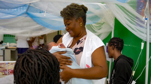 Naomie Lubin, an MSF midwife at the Isaïe Jeanty maternity hospital in Port-au-Prince, smiles while holding a newborn in her arms, a few hours after their birth.  Naomie herself was born in that same maternity, 49 years ago.   

Chancerelles, Port-au-Prince, Haiti. March 2026.