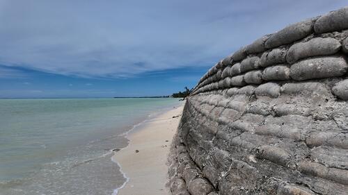 A sea wall shores up against the sea in Tarawa, Kiribati's capital. Kiribati faces rising sea levels and increasingly unpredictable weather events due to climate change.  Kiribati (pronounced Ke-ree-bas) is a vast but climate-vulnerable island nation made up of 32 atolls and one raised coral island in the Pacific. It lies half-way between Hawaii and Australia. With a total land mass of just 811 square km spread over 3.5 million square km of ocean, the country has unique social and geographical challenges. The increase in frequency and intensity of storms and other extreme weather events, the intrusion of salt water with a rising sea, along with declining rainfalls and higher temperatures, threaten ecosystems and are rapidly deplete freshwater supplies