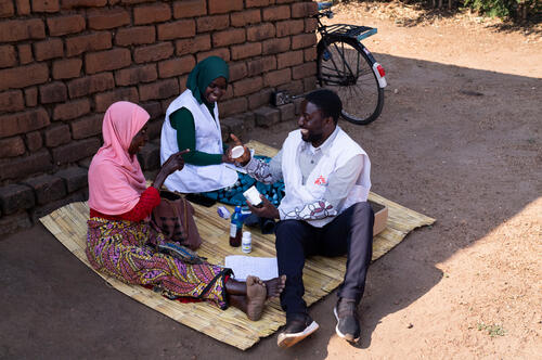 Two members of the MSF palliative care team, Wilfred Nkhambule and Vitu Mwanza, palliative care nurses,  go over Jean Gama's medication during a home visit in Nkando, in Mulanje district, Malawi, on July 22, 2026. The team taught her to apply her treatments herself and withdraws those she tolerates poorly.
