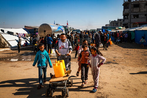 Youssef Al-Khishawi, an MSF water and sanitation agent, helps children carry water to their tent in the Tal Al-Sultan area of the southern Gaza town of Rafah, on January 27, 2024.